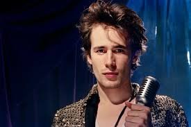 Cantante Jeff Buckley sosteniendo un micrófono vintage frente a un fondo azul, famoso por su álbum "Grace"